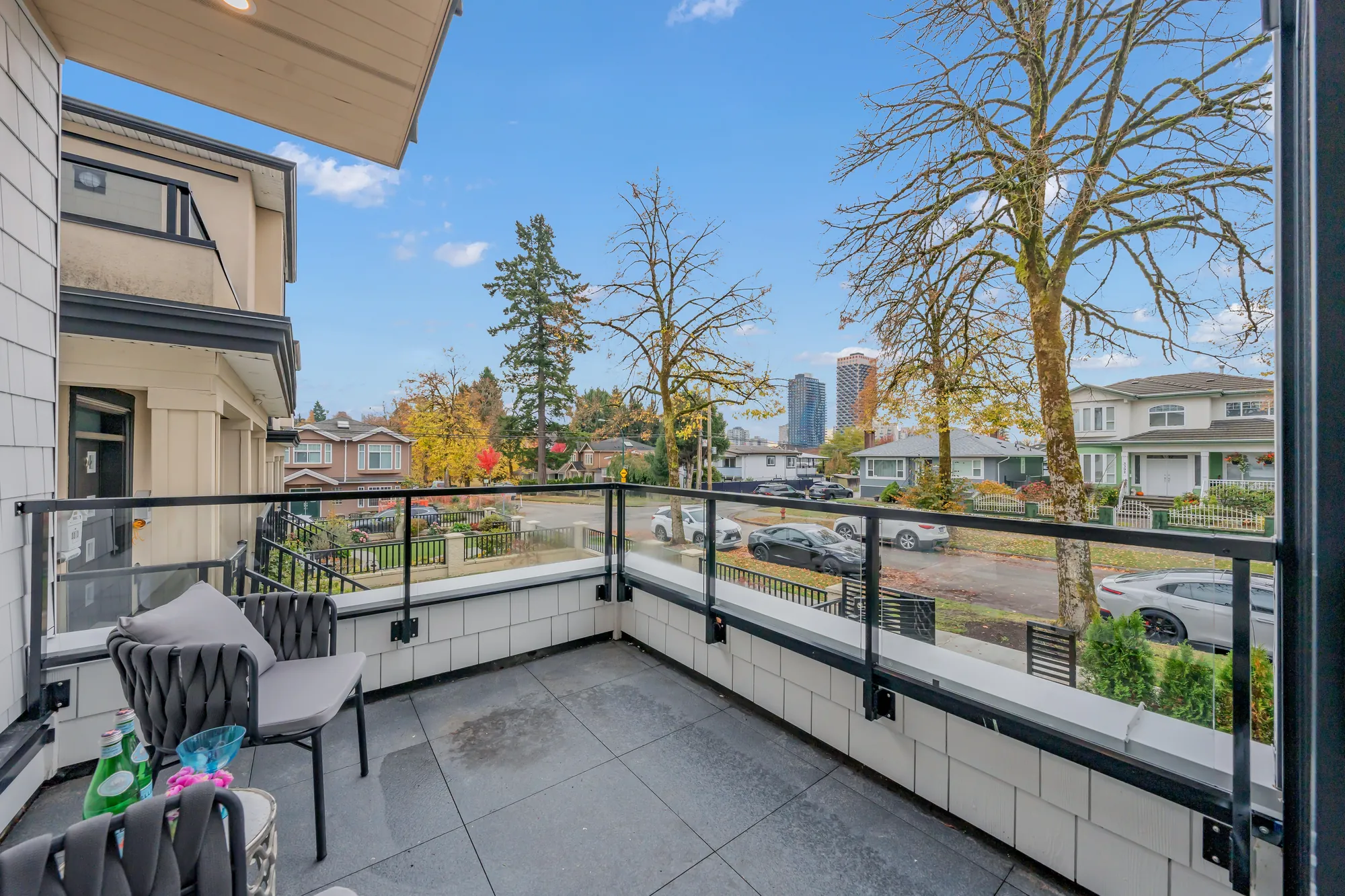 The balcony off the living room: grey pavers, a glass and steel railing, two woven chairs, the street and towers beyond