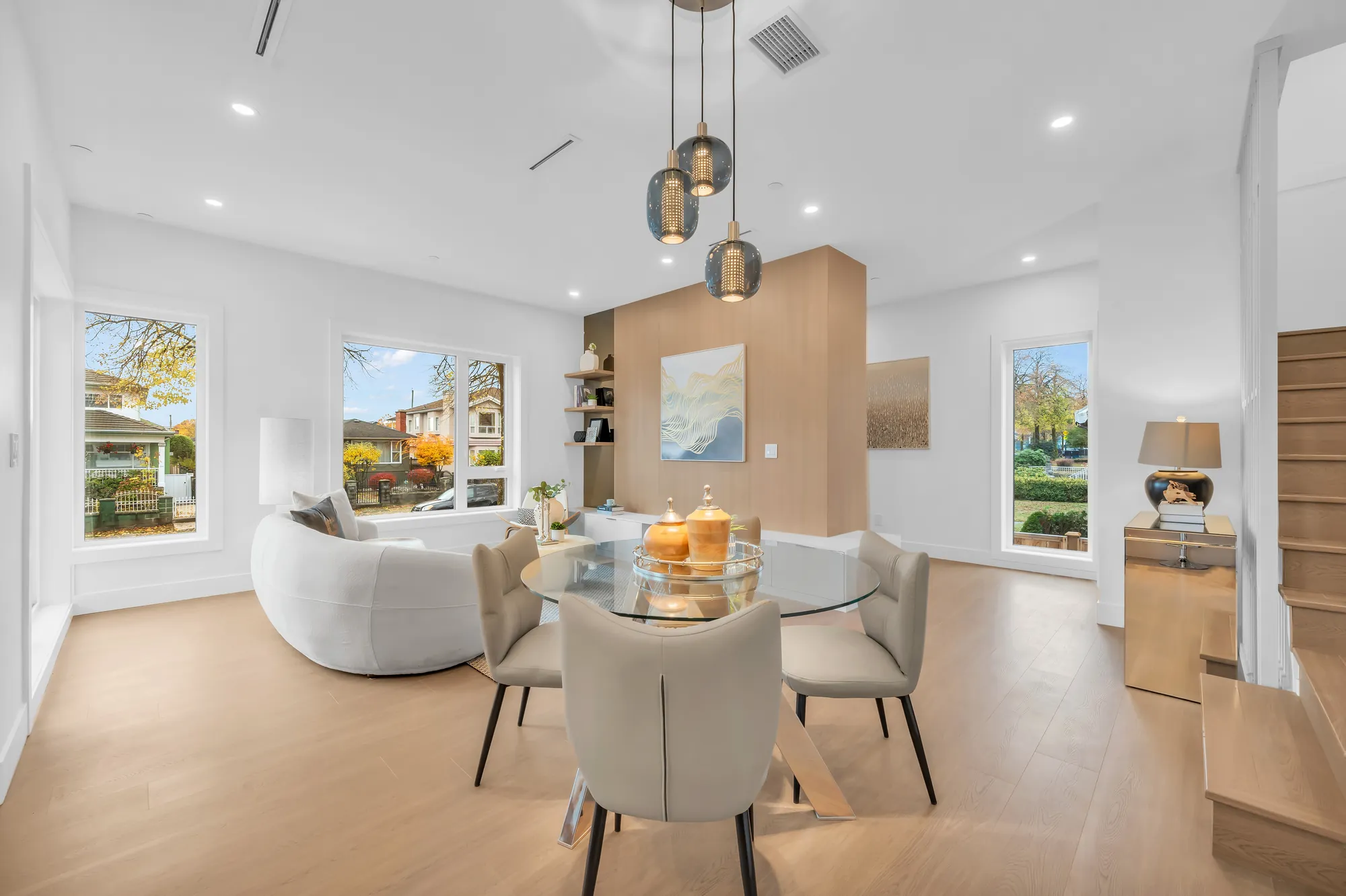 The dining room: a round glass table and four upholstered chairs under three glass pendants, windows to the front and the side