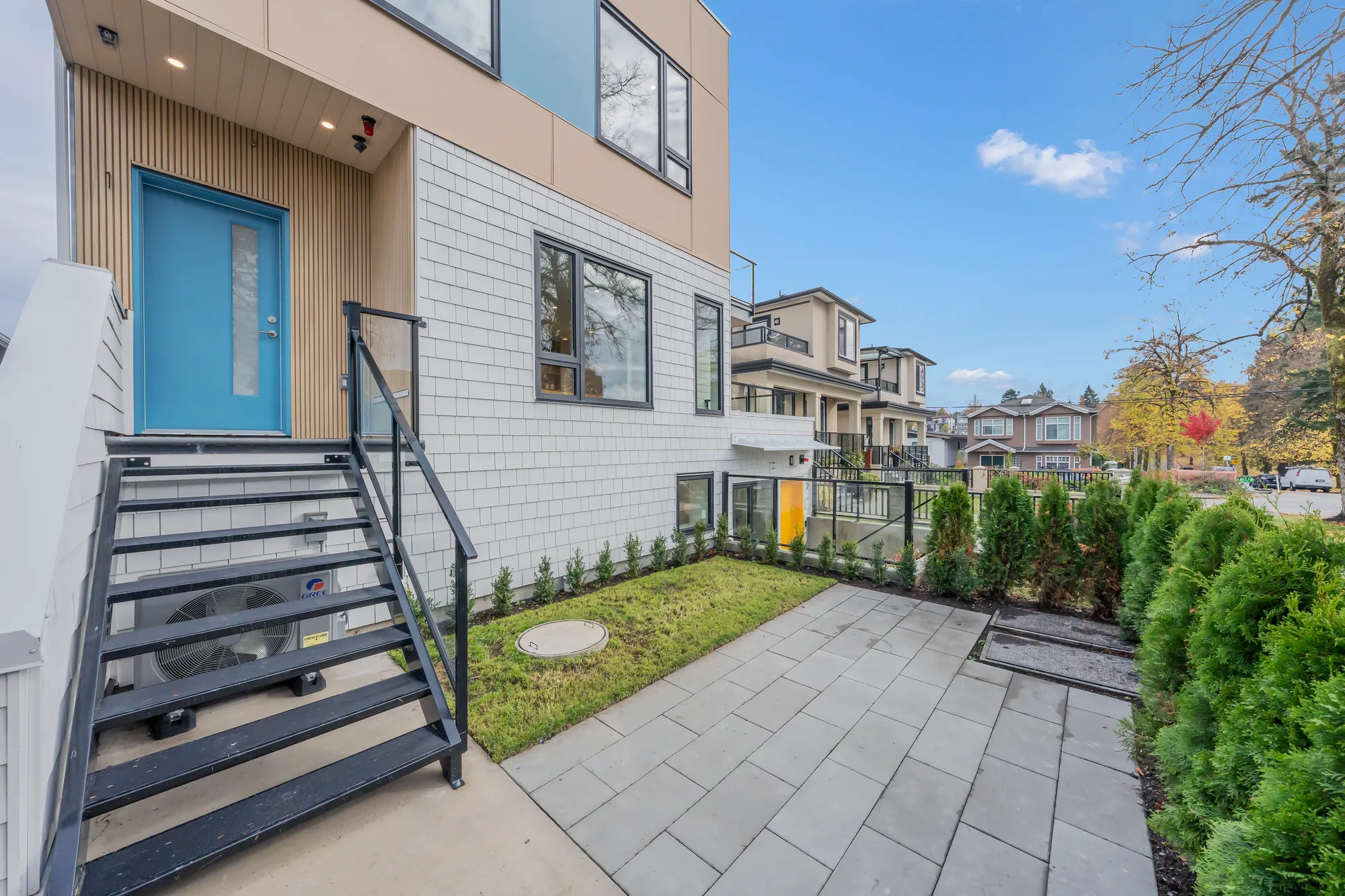 #1's front door, blue-green, at the top of a flight of black steel steps, a strip of lawn and pavers below