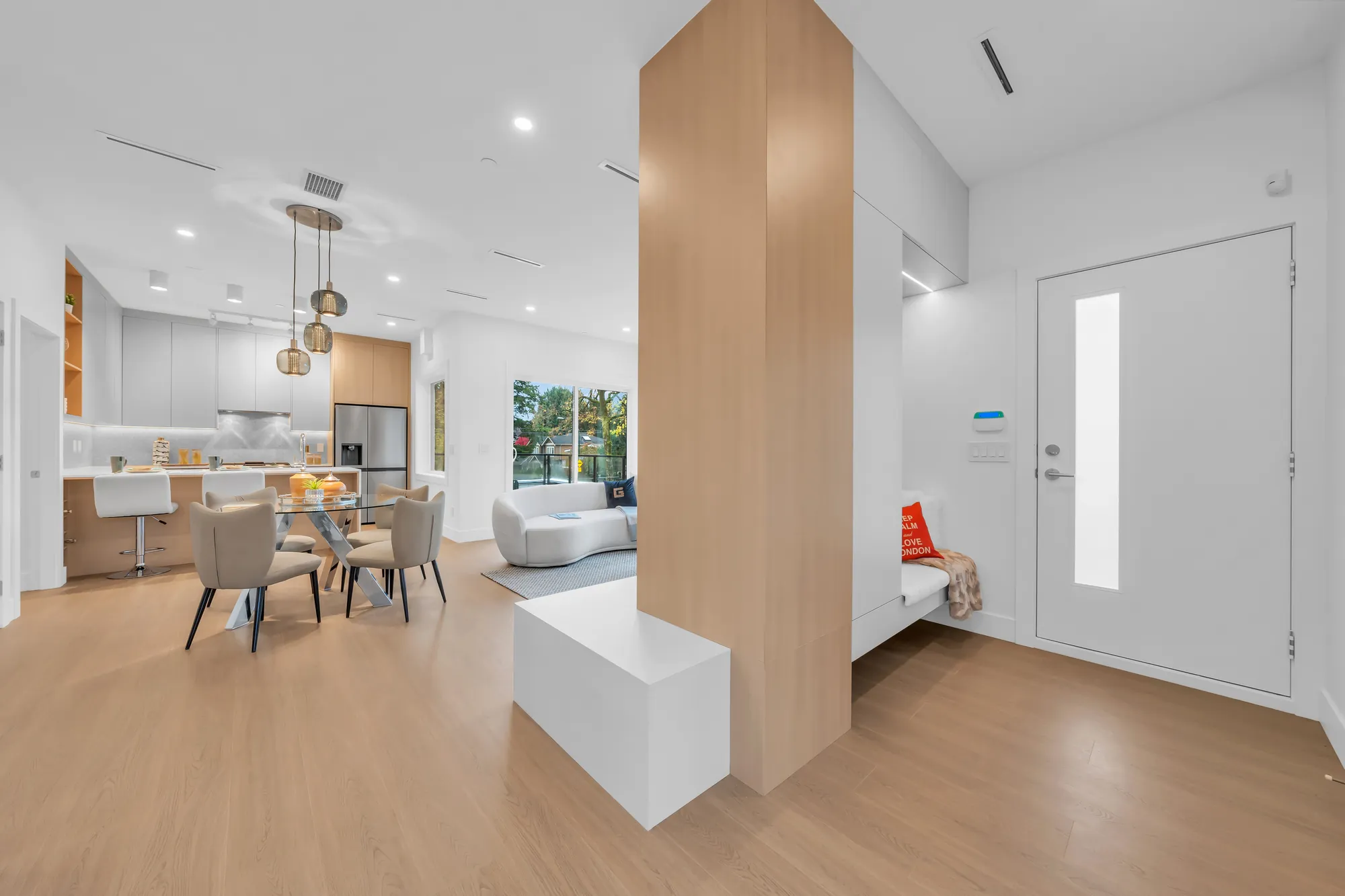 From the front door to the dining room and the kitchen: an oak-clad column, a round glass table under glass pendants, the kitchen at the back