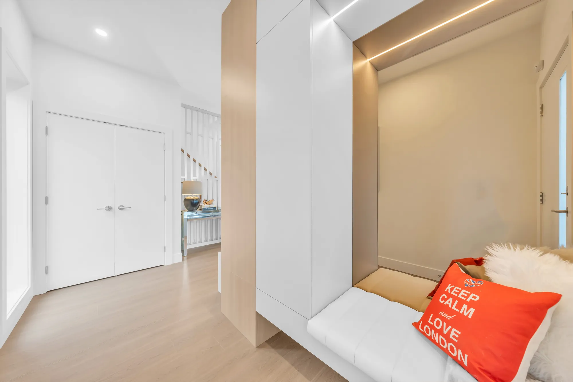 A built-in bench with a cushion in a lit oak niche, white double closet doors across the hall