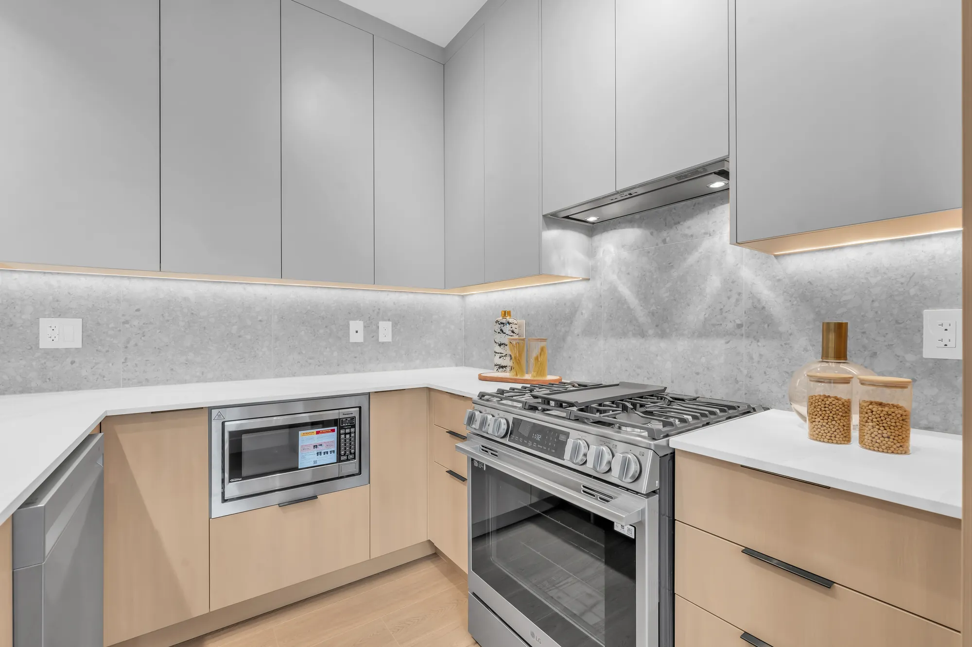 A stainless range under a hood, a grey stone backsplash, the microwave in an oak cabinet