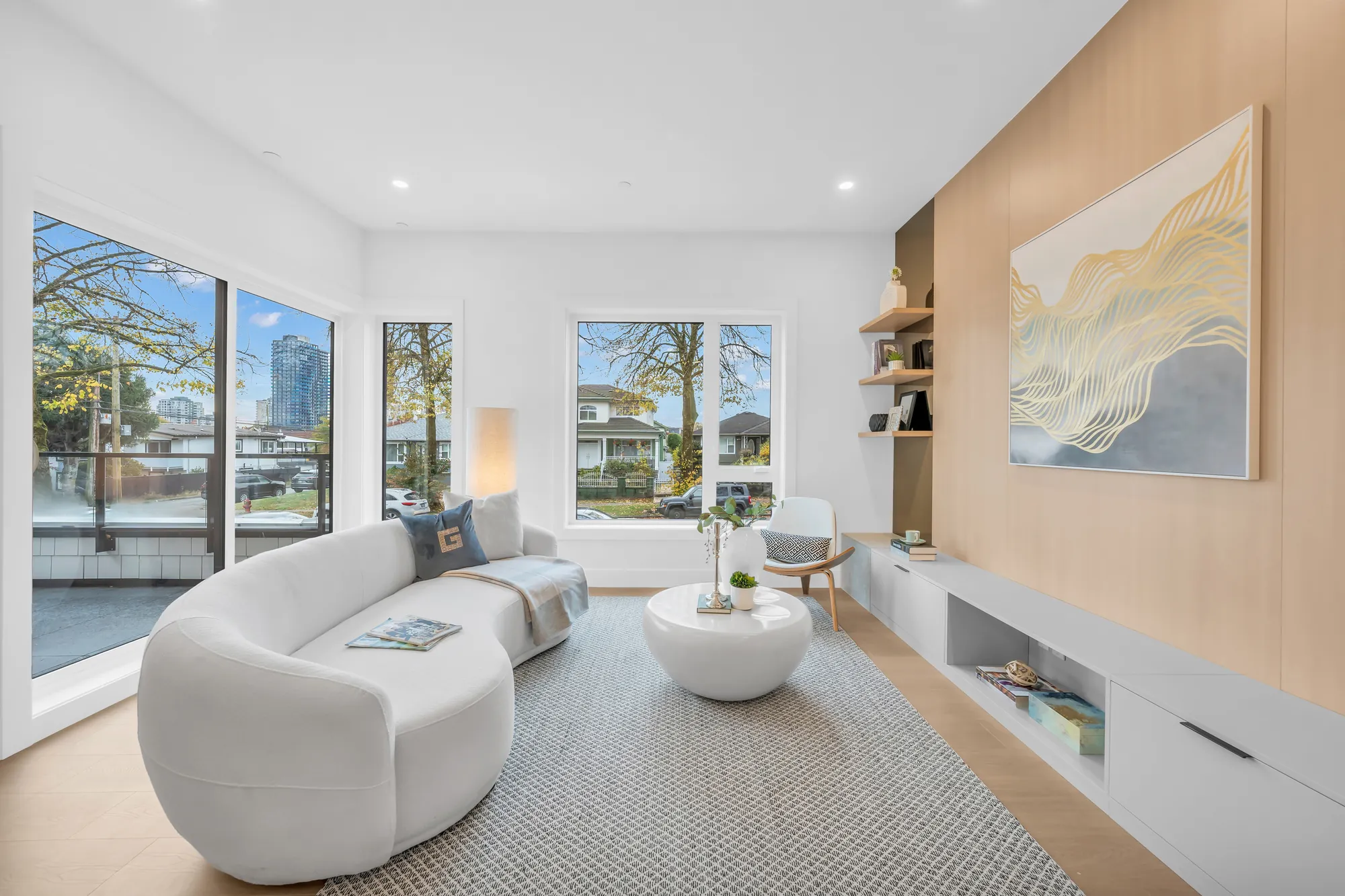 The living room: a white curved sofa, a low white media unit and an oak wall with a framed print, a glass door to the balcony