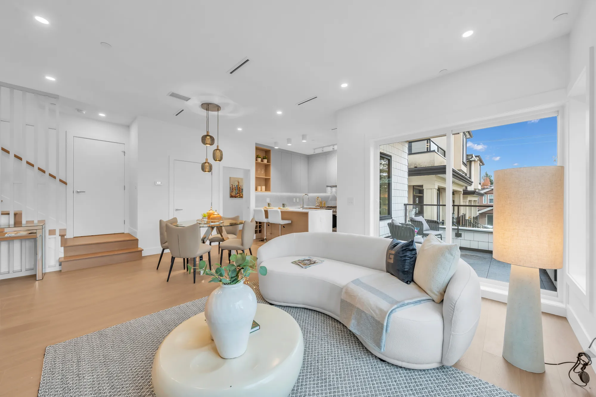 The living room toward the dining room and the stair, a tall floor lamp, the balcony door