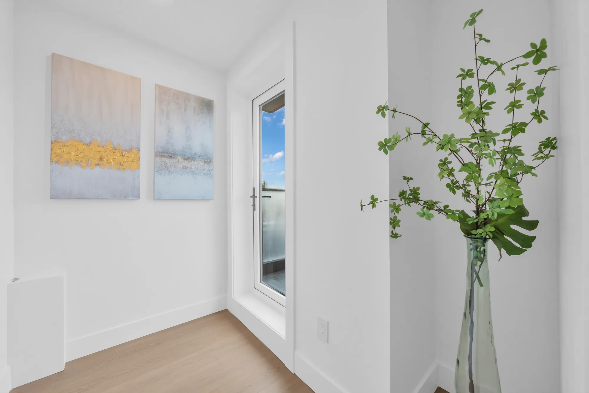 The loft at the top of the stair: white walls, framed prints, a tall plant, a glass door to the roof terrace