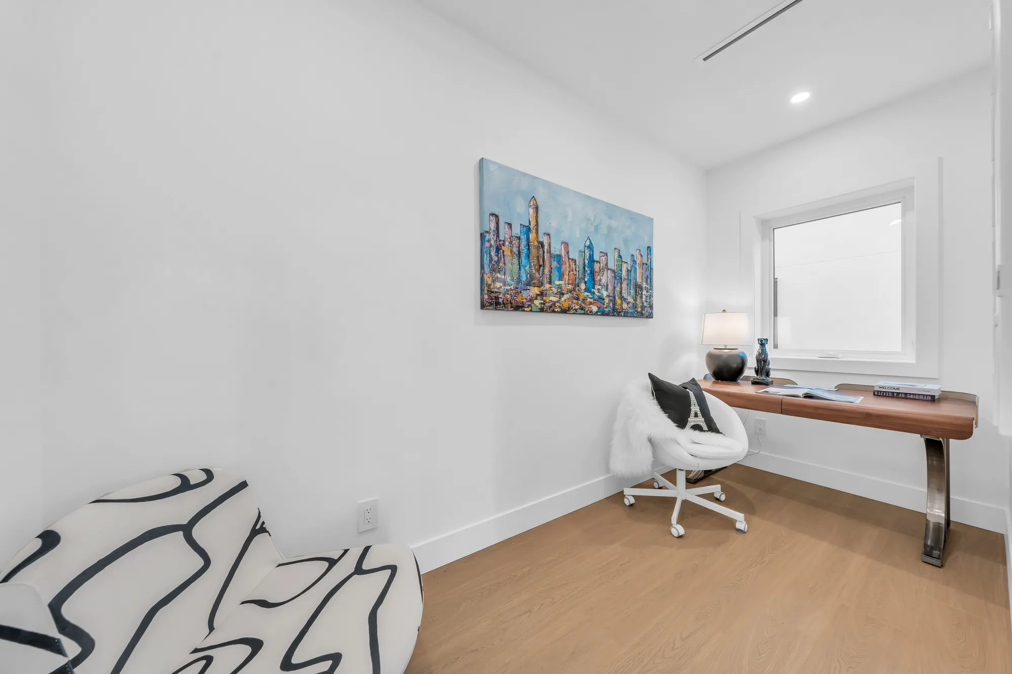 The office: a wood desk and a white chair, a framed print of a skyline, a window
