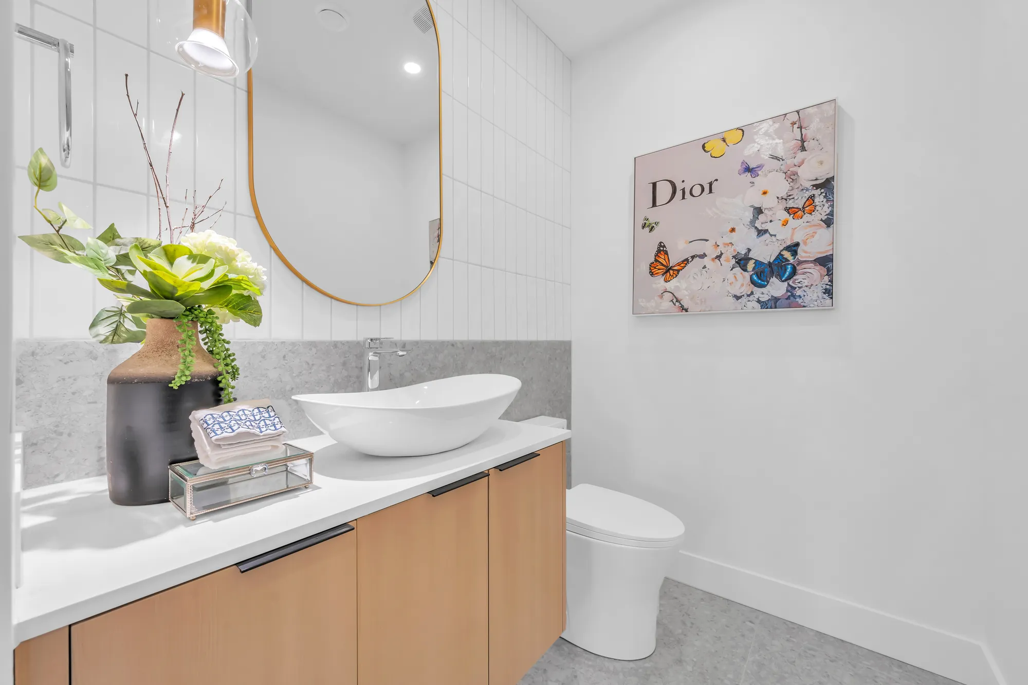 The powder room: a white vessel sink on an oak vanity with a stone top, an oval brass mirror, a toilet