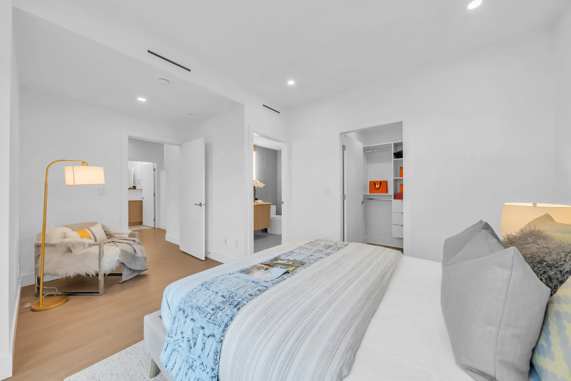 The primary bedroom toward the walk-in closet and the bathroom: the bed, a floor lamp and an armchair