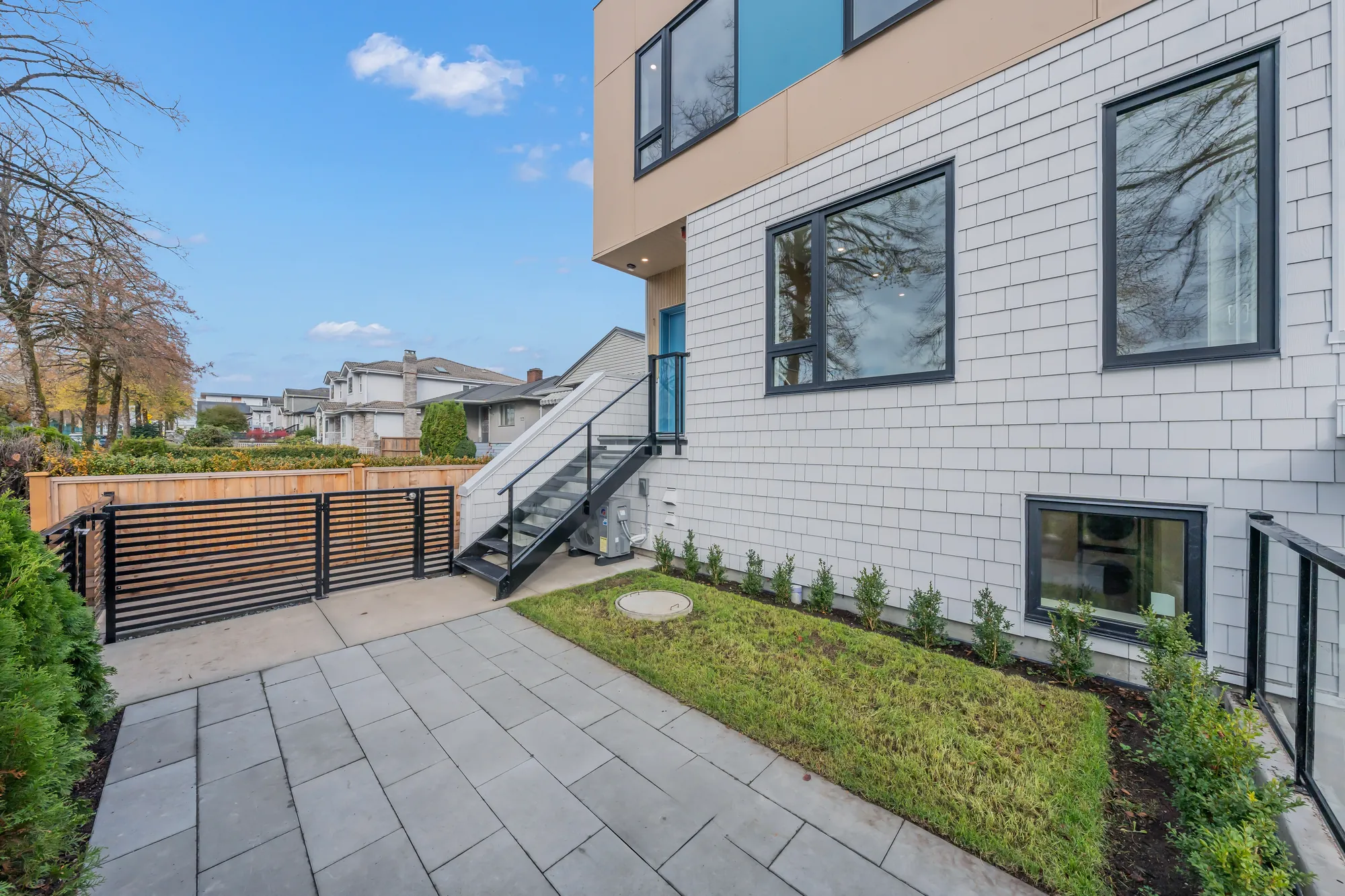 The front yard: grey pavers and a strip of lawn inside a black slatted gate, the steps up to #1