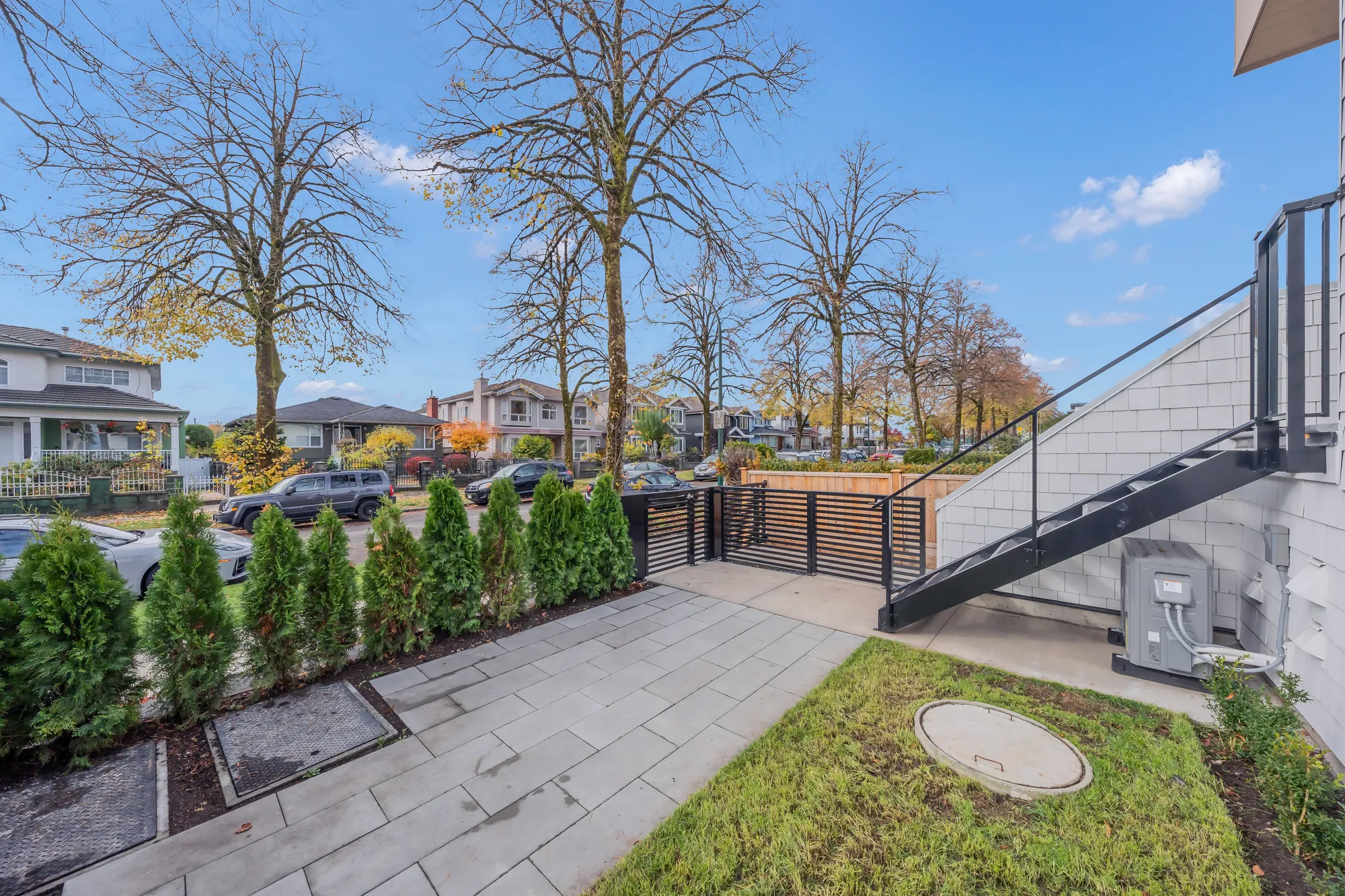 The front yard toward the street: pavers, lawn, the cedar hedge and the gate, #1&rsquo;s stair at the right